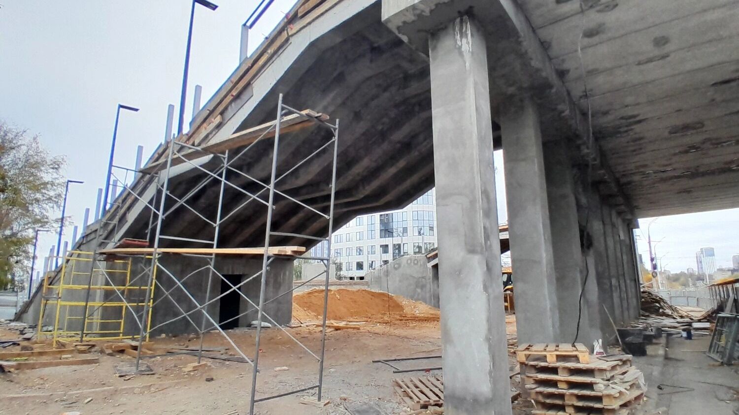 Около моста стоят строительные леса, строители обновляют западный лестничный сход